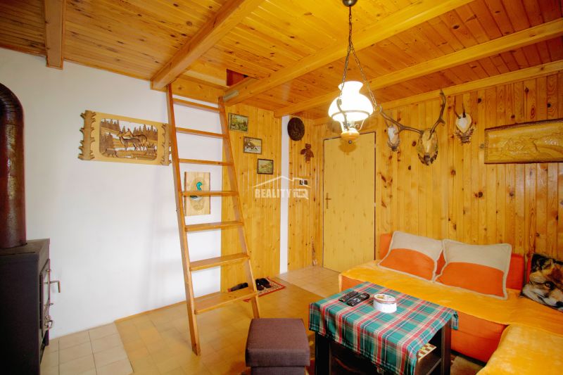 Holzinterieur der Hütte mit Leiter und Kaminofen, ergänzt durch Jagddekor.