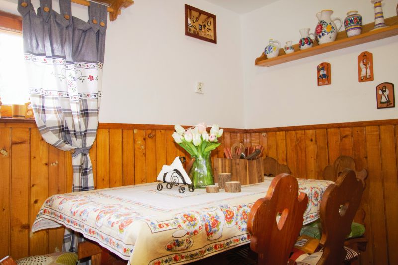 Innenraum einer Hütte mit Tisch, rustikaler Dekoration und Holzverkleidung an den Wänden.