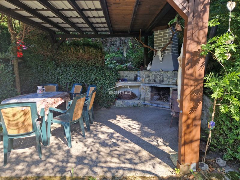 Überdachte Terrasse mit Kamin neben einer Hütte bei Žilina, umgeben von Grün und Sitzgelegenheiten.