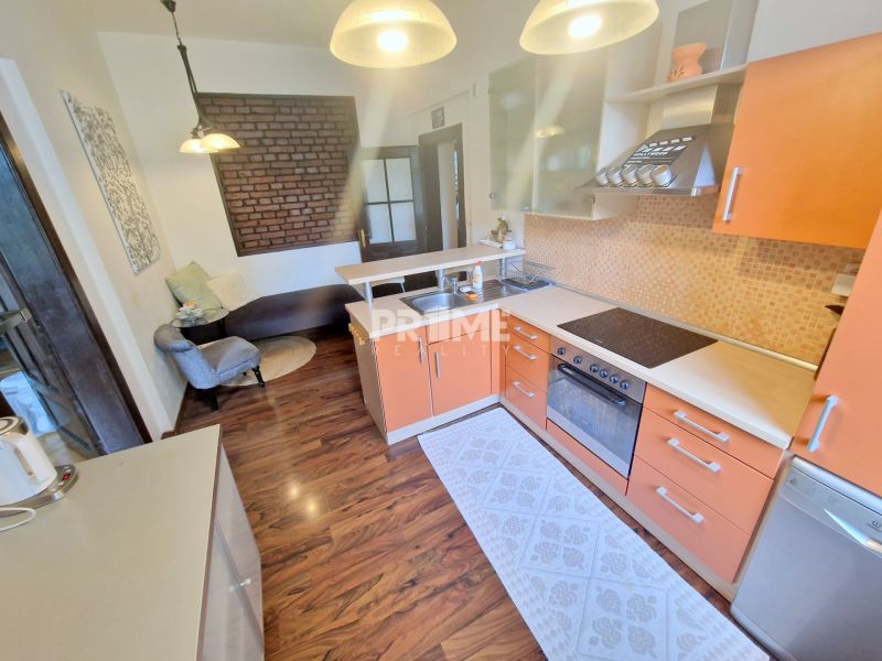 Küche mit orangefarbener Küchenzeile, Sofa und Boden mit Holzdekor in einer 3-Zimmer-Wohnung.