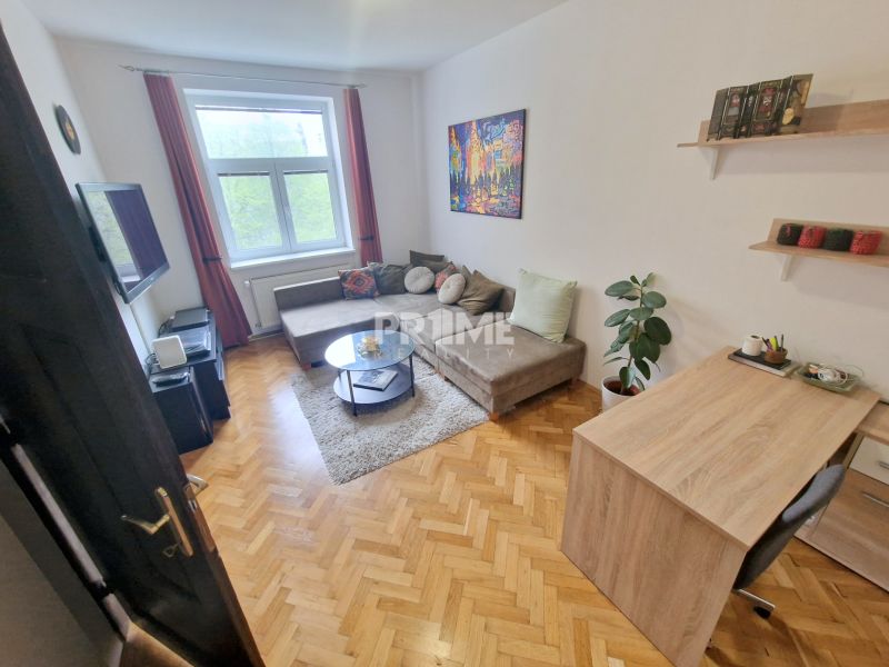 Ein Zimmer in einer 3-Zimmer-Wohnung mit einem Sofa, einem Fernseher und einem Boden in Holzoptik.