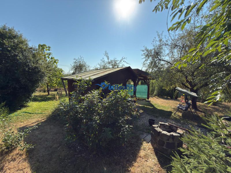 Die Hütte im Weingarten in Lučenec, umgeben von Grün und Bäumen, mit einer Feuerstelle im Garten.