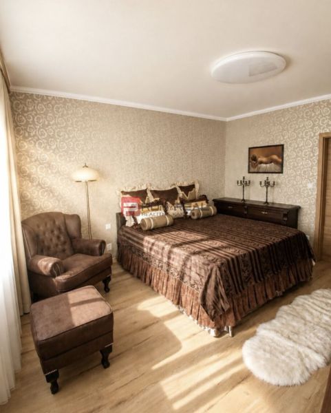 Schlafzimmer mit Sessel und Bett, Holzboden, warme Farbtöne.