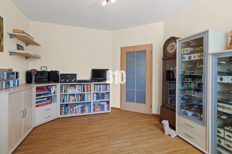 Ein Zimmer in einer 4-Zimmer-Wohnung mit Regalen, Schränken, Büchern und einem Boden in Holzoptik.