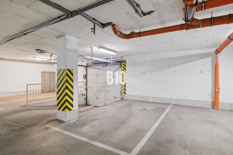 Unterirdischer Parkplatz in einer 4-Zimmer-Wohnung mit gelben Sicherheitsstreifen und Rohrleitungen.