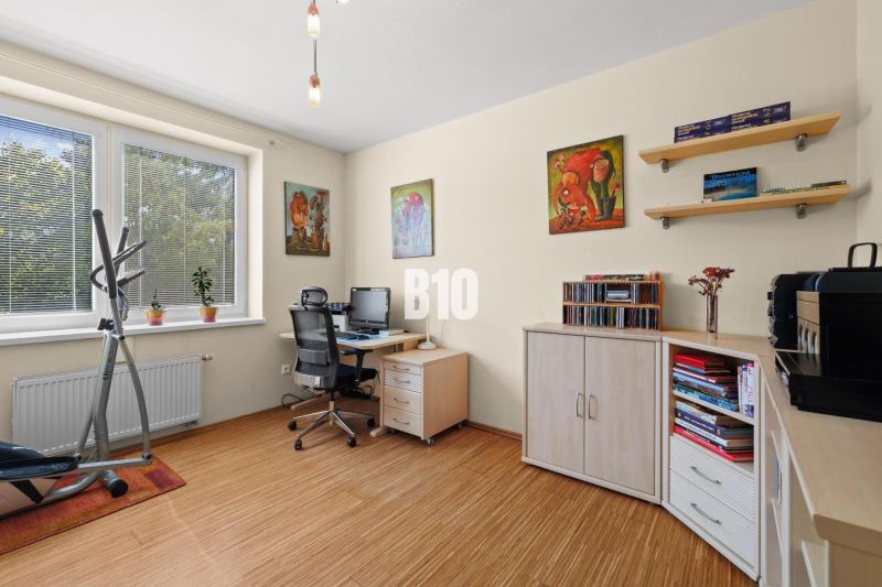 Ein Arbeitszimmer mit einem Tisch, Blumen und einem Fitnessgerät in einer 4-Zimmer-Wohnung mit einem Boden in Holzoptik.