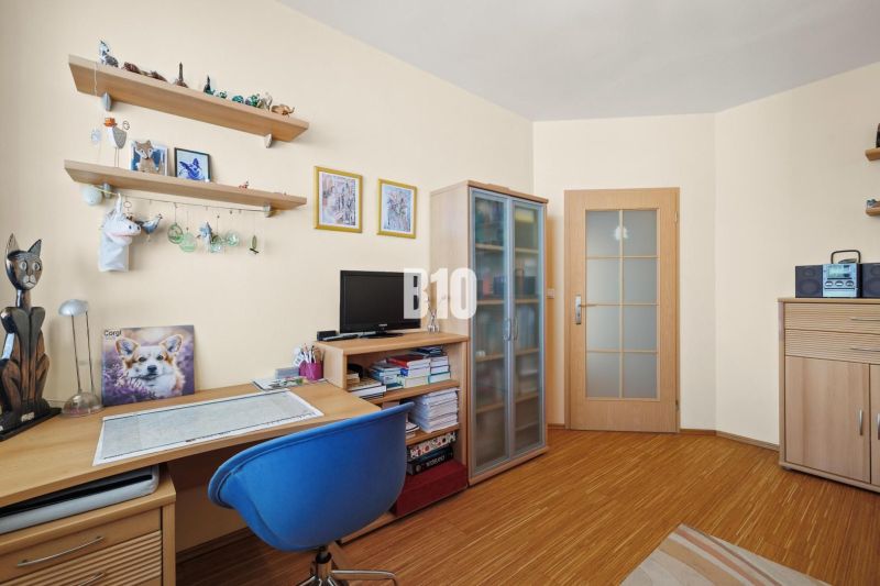 Ein Arbeitszimmer in einer 4-Zimmer-Wohnung mit Regalen, Holzmöbeln und einem Boden in Holzoptik.