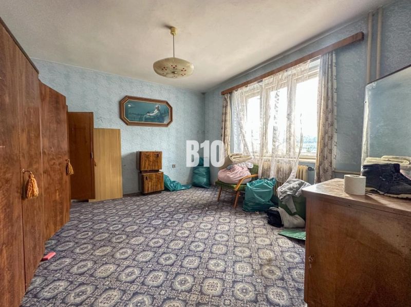 Ein Zimmer in einem Einfamilienhaus mit Teppich, Schränken und einem Sessel unter dem Fenster.