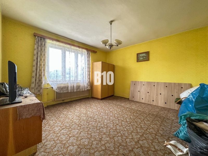 Ein Zimmer in einem Einfamilienhaus mit Teppich, Möbeln und Vorhängen am Fenster.