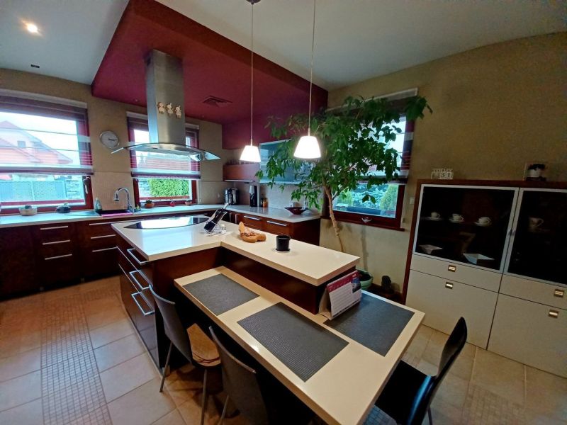 Eine Küche in einem Einfamilienhaus mit einer Insel, einem Esstisch und großen Fenstern für viel Licht.