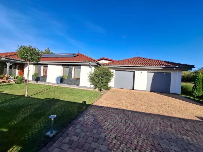 Ein Einfamilienhaus in Nové Zámky mit rotem Dach, Garage und gepflegtem Rasen.
