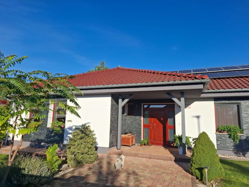 Ein Einfamilienhaus in Nové Zámky mit rotem Dach, Solarpaneelen und Garten.