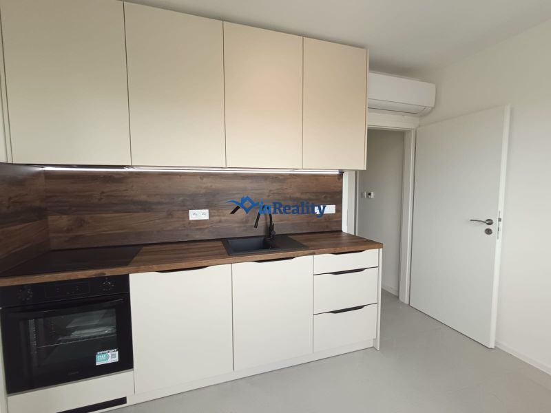Küche in einer 2-Zimmer-Wohnung mit weißen Schränken und Holzboden.