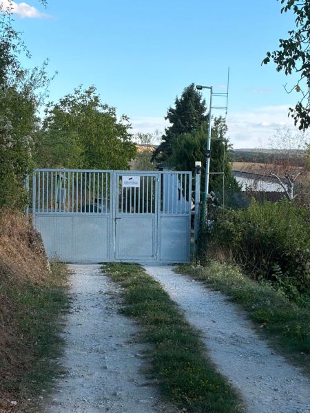 Das Tor, das zur Hütte in Banka führt, umgeben von Grün und einem Feldweg.