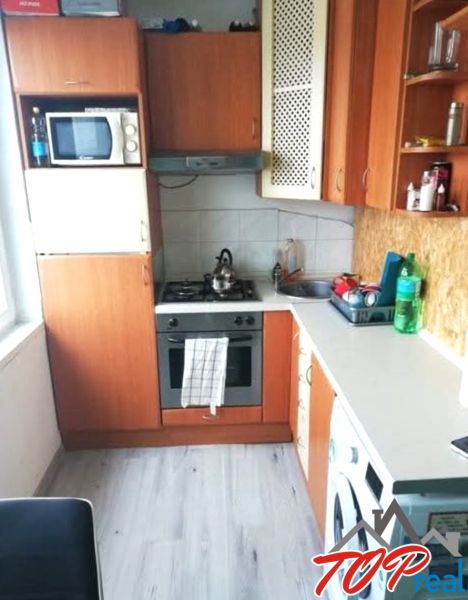 Küche in einer Einzimmerwohnung mit Holzboden, grundlegenden Geräten und Schränken.