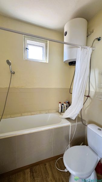 Badezimmer mit Badewanne, Dusche, Boiler und Boden mit Holzdekor in einem Einfamilienhaus.