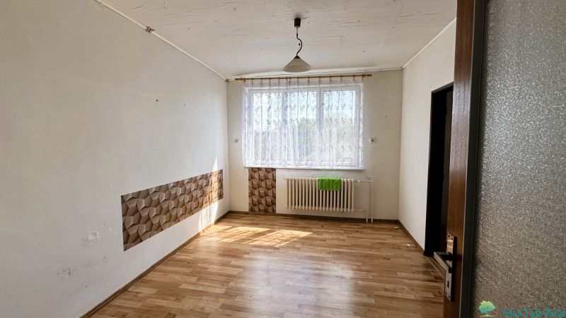 Ein Zimmer in einem Einfamilienhaus mit einem Boden in Holzoptik, einem Vorhang und einem Heizkörper unter dem Fenster.