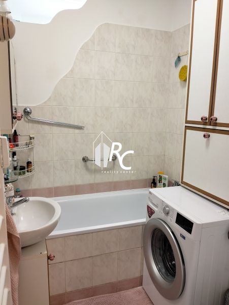 Badezimmer in einer Einzimmerwohnung mit Badewanne und Waschmaschine, gefliest mit hellen Fliesen.
