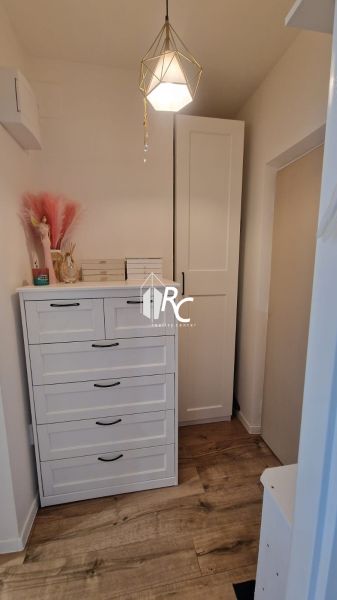 Ein Zimmer in einer Einzimmerwohnung mit einer Kommode, einem Kleiderschrank und einem Boden in Holzoptik.