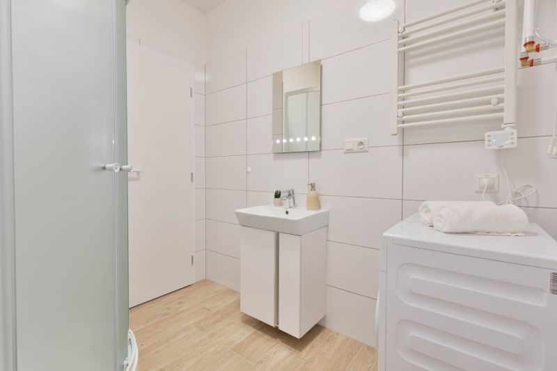 Badezimmer in einem Studio-Apartment mit Holzboden, weißen Fliesen und einer Duschkabine.