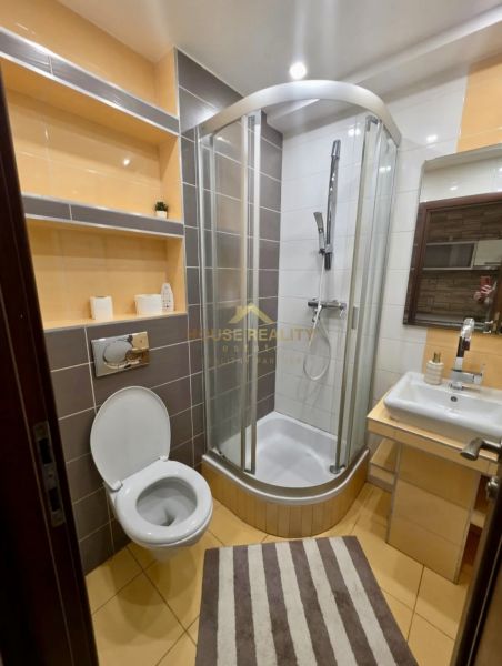 Badezimmer mit Toilette, Duschkabine, Waschbecken und Regalen in einer Einzimmerwohnung.