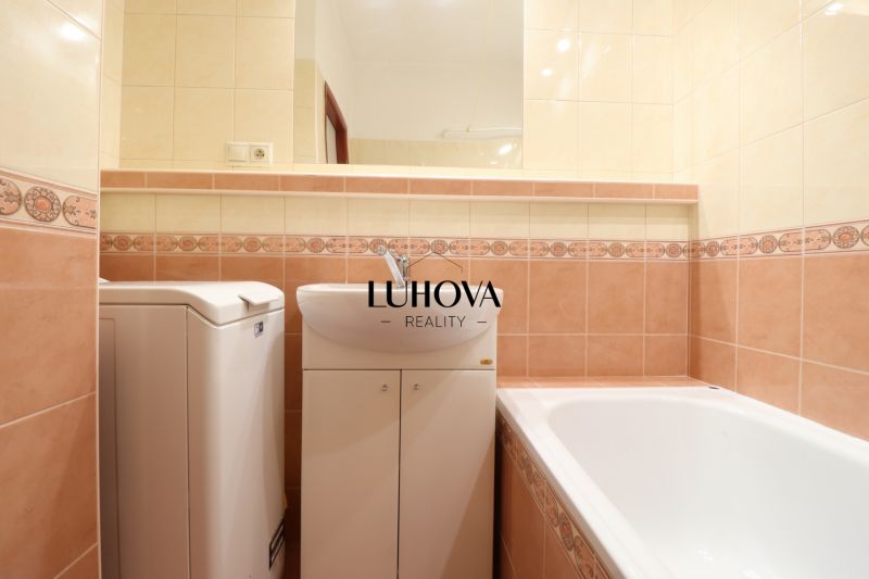 Badezimmer in einer 2-Zimmer-Wohnung mit Badewanne und Waschmaschine, gefliest mit bunten Fliesen.