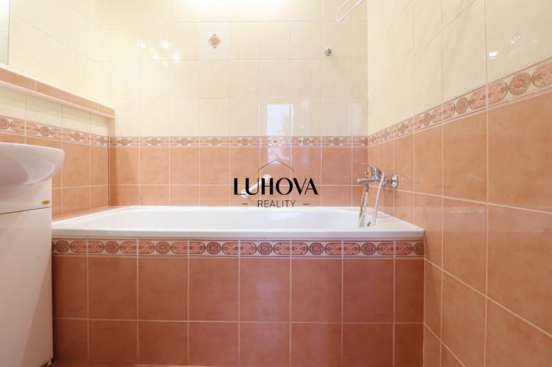 Badezimmer in einer 2-Zimmer-Wohnung mit Badewanne und Waschbecken, gefliest mit beige- und rosafarbenen Fliesen.
