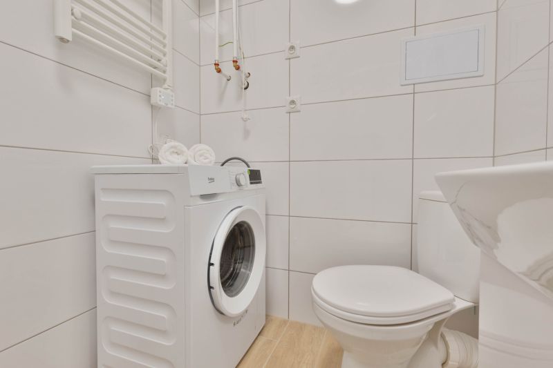 Badezimmer in einem Studio-Apartment mit Waschmaschine, Toilette und Holzboden.