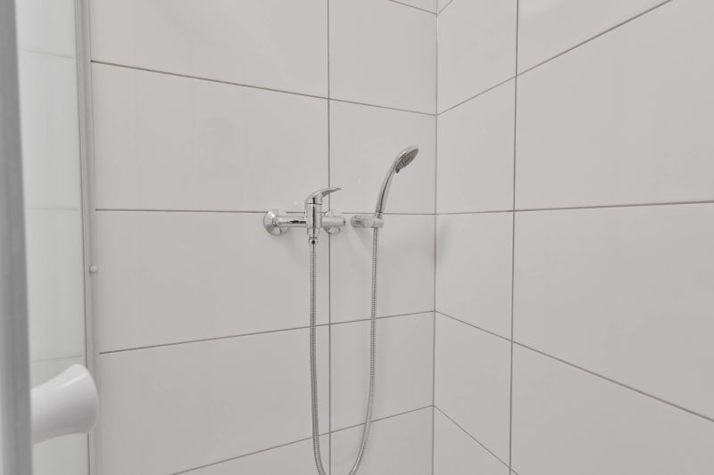Duschkabine mit weißen Fliesen und Duschkopf in einem Einzimmerapartment.