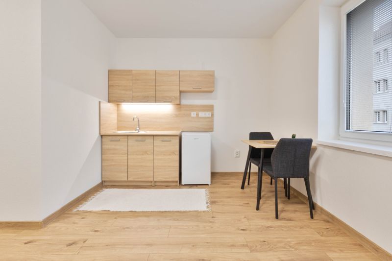 Einzimmerwohnung mit Küchenzeile, Kühlschrank und Tisch, ergänzt durch einen Boden mit Holzdekor.