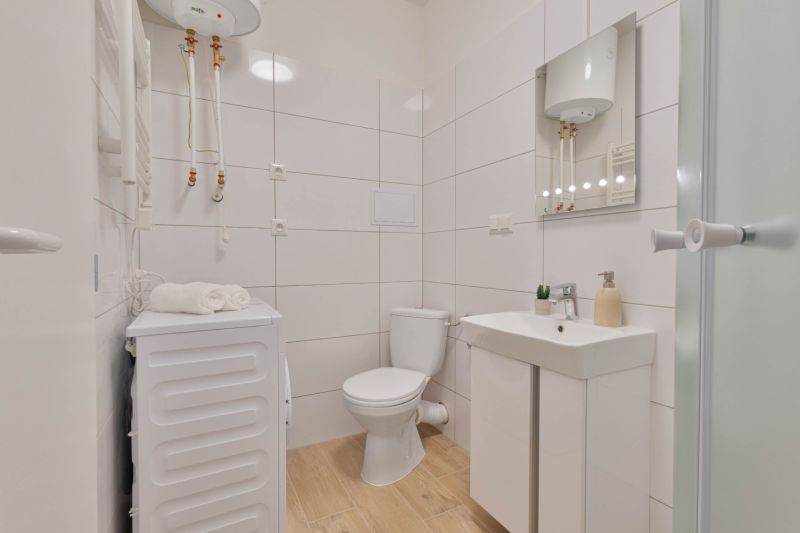Badezimmer in einem Einzimmerapartment mit Waschmaschine, Toilette, Waschbecken und Boiler, Boden mit Holzdekor.
