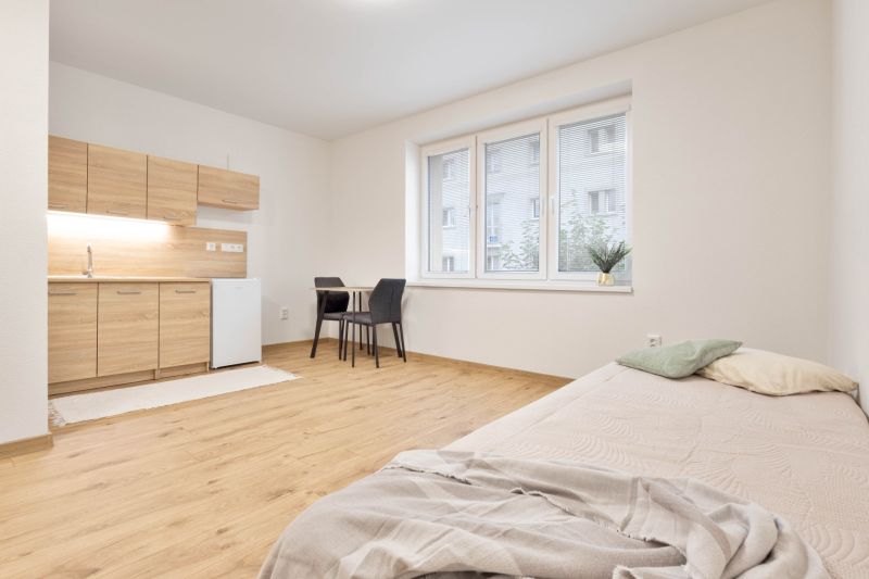 Einzimmerwohnung mit Kochnische, Bett und Esstisch, Boden mit Holzdekor.