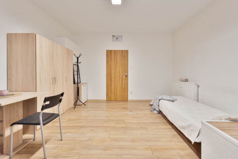 Einzimmerwohnung mit Bett, Schrank, Tisch und Boden in Holzoptik.