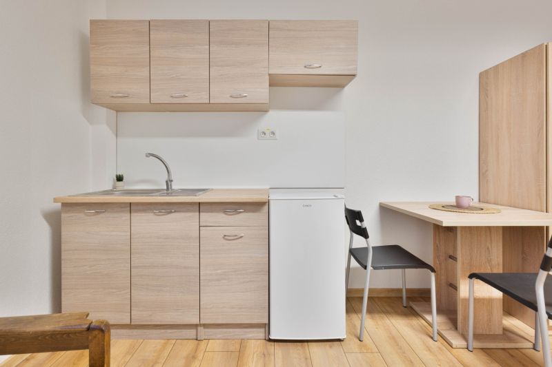 Küchenbereich in einem Einzimmerapartment mit weißem Kühlschrank und Holzboden.