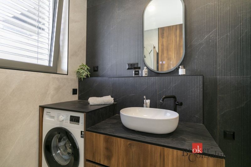 Badezimmer einer Zweizimmerwohnung mit Waschbecken, Waschmaschine und Spiegel.