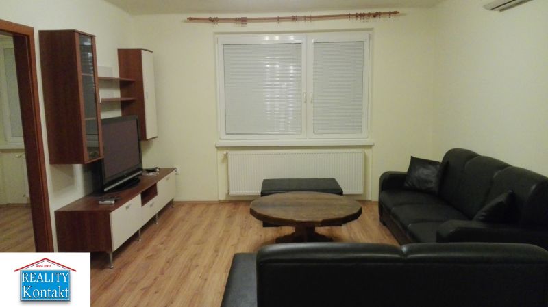 Wohnzimmer in einer 3-Zimmer-Wohnung mit Holzdekorboden und schwarzem Sofa.