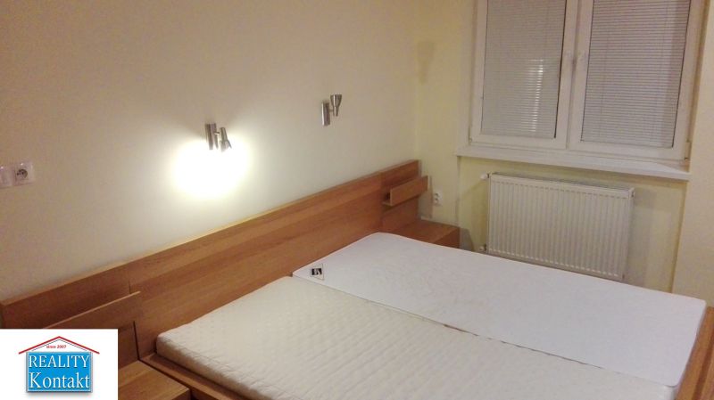 Schlafzimmer einer 3-Zimmer-Wohnung mit einem Holzbett und einem Fenster mit Rollläden an der Wand.