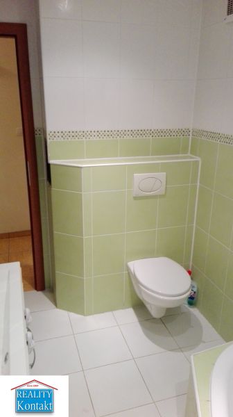 Badezimmer mit weißen und grünen Fliesen in einer 3-Zimmer-Wohnung, WC und Waschbecken.