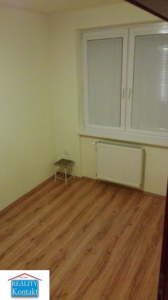 Ein Zimmer in einer 3-Zimmer-Wohnung mit einem Boden in Holzoptik und weißen Fenstern.