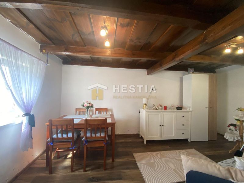 Wohnzimmer in einem Einfamilienhaus mit Holzdecken, weißer Kommode und Vorhängen.
