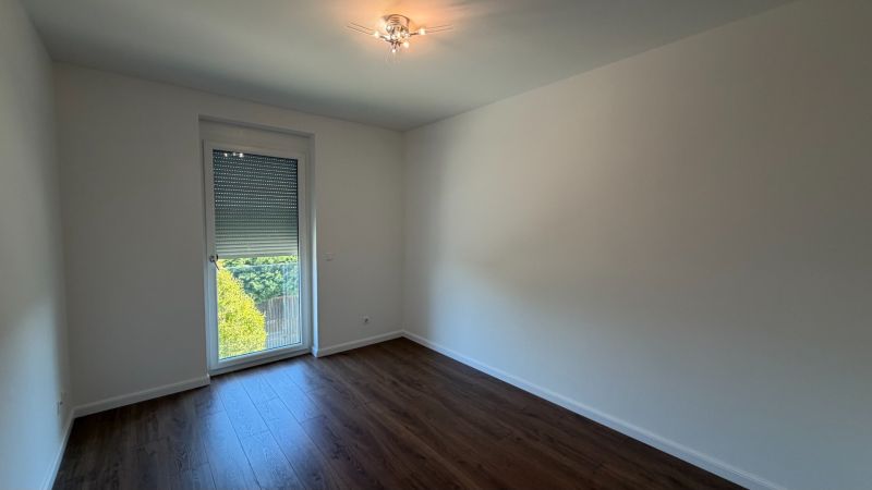Ein Zimmer in einer 3-Zimmer-Wohnung mit weißen Wänden und einem Boden in Holzoptik.