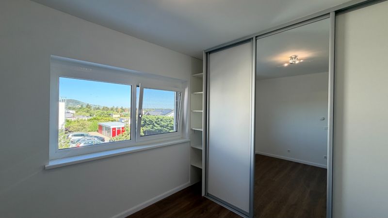 Ein Zimmer mit einem Einbauschrank, einem Boden in Holzoptik, einem großen Fenster mit Ausblick.