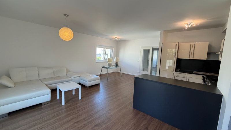 Wohnzimmer in einer 3-Zimmer-Wohnung mit weißem Sofa und Boden in Holzoptik.