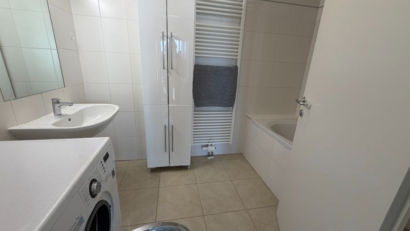 Badezimmer in einer 3-Zimmer-Wohnung mit Waschmaschine, Waschbecken und Badewanne auf hellen Fliesen.