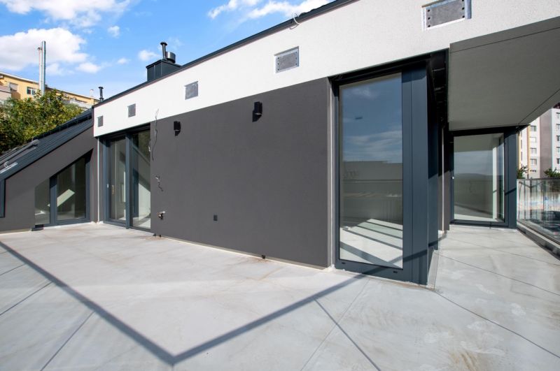 Geräumige Terrasse einer 5- oder mehr Zimmer-Wohnung mit moderner Fassade und Glasgeländer.