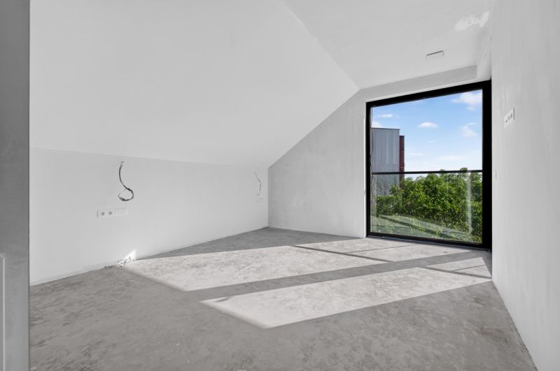 Ein Zimmer mit einem großen Fenster und grauem Boden in einer Mehrzimmerwohnung.