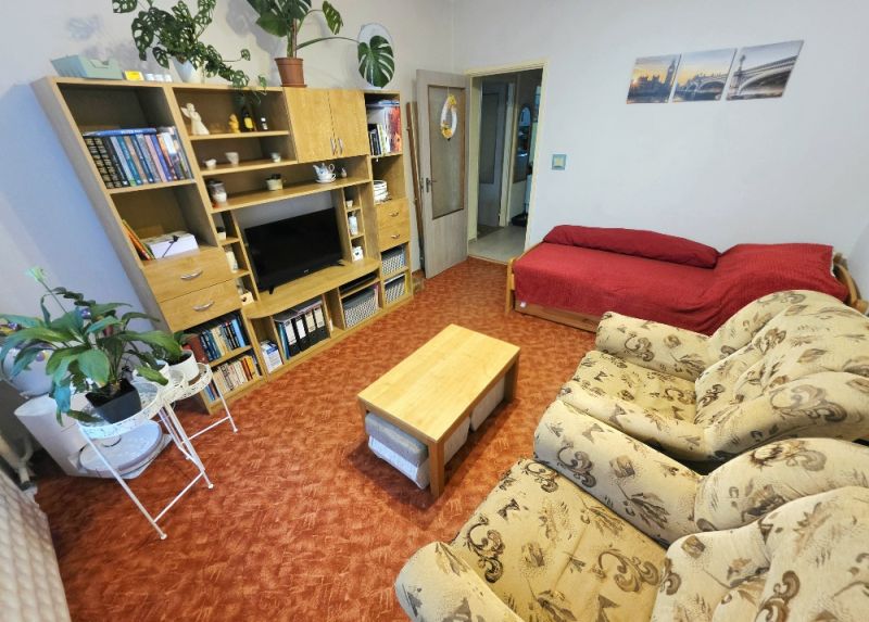 Wohnzimmer in einer 4-Zimmer-Wohnung mit Sofa, roter Sitzecke und Wandregal.