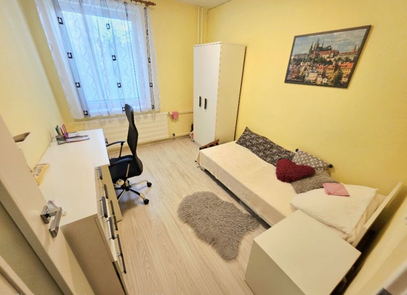 Ein gelbes Zimmer mit einem Einzelbett, einem Schreibtisch und einem Boden in Holzoptik in einer Vierzimmerwohnung.