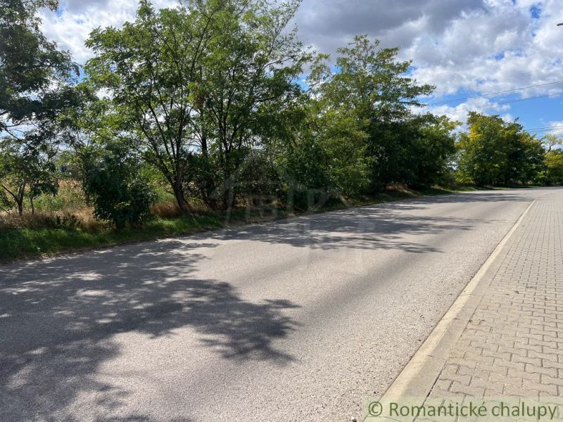 Eine Straße in Bernolákovo, umgeben von Grünflächen auf landwirtschaftlichen und forstwirtschaftlichen Grundstücken, blauer Himmel.