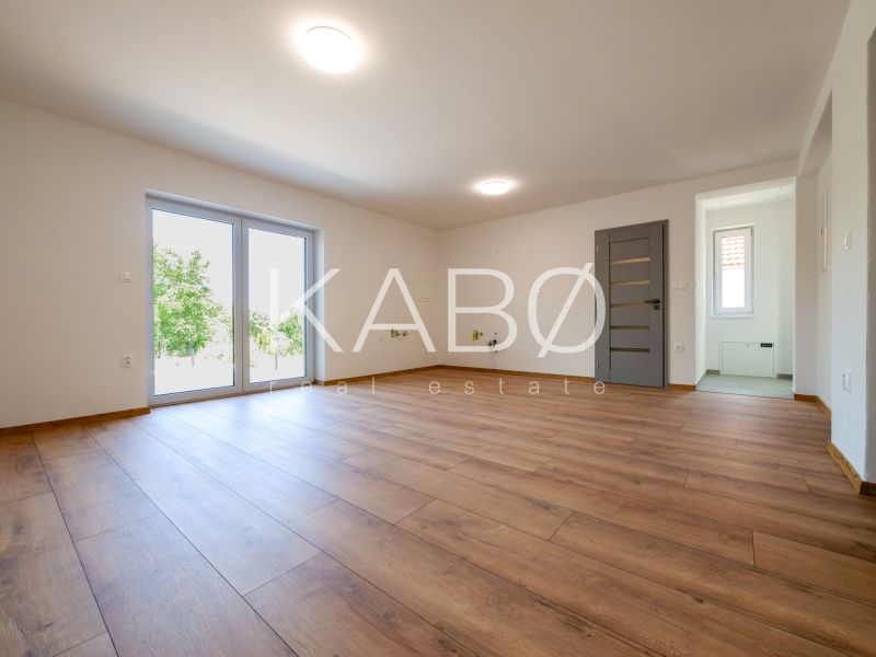 Wohnzimmer in einem Einfamilienhaus mit großen Fenstern und einem Boden in Holzoptik.